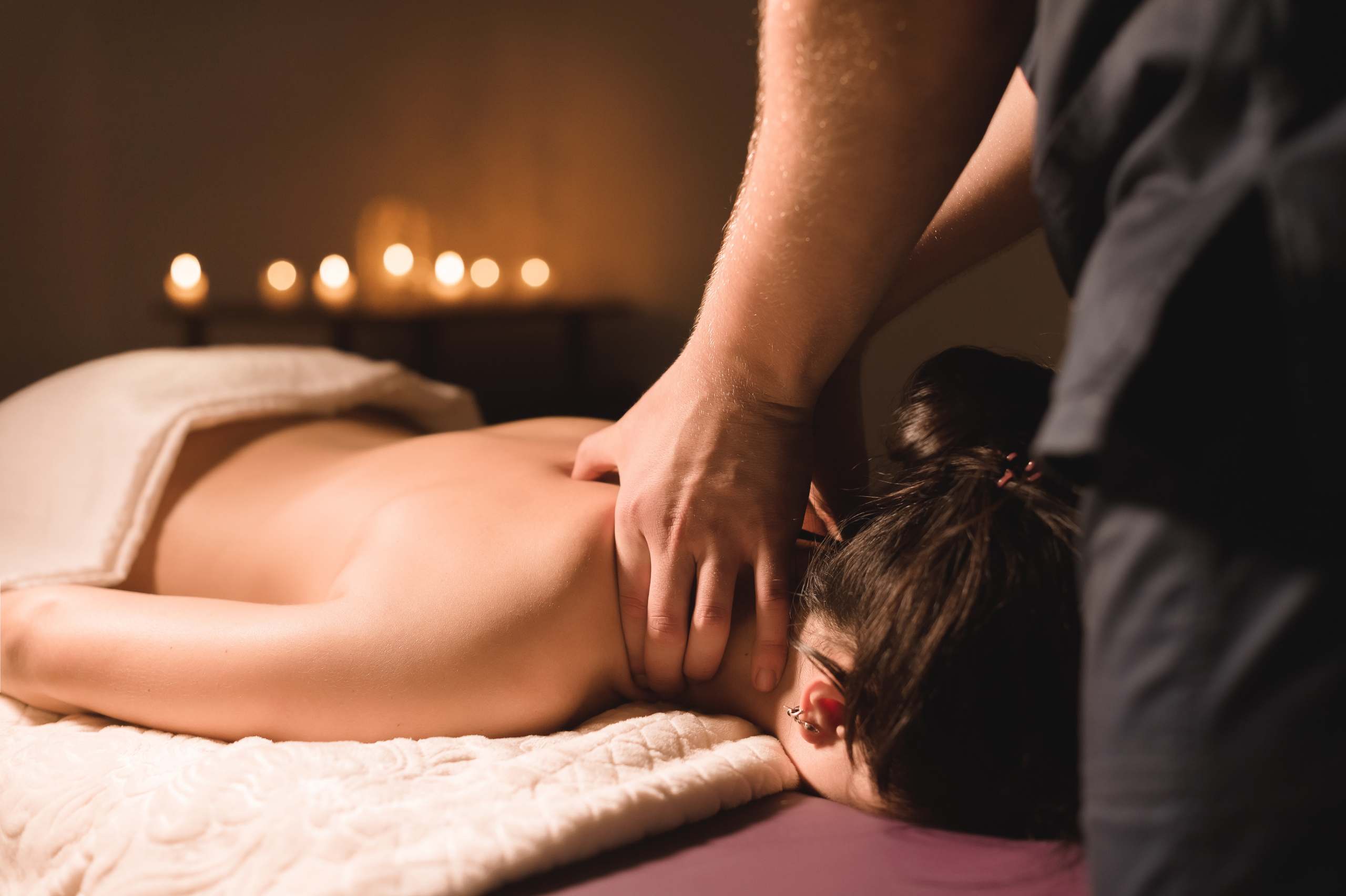 Men’s hands make a therapeutic neck massage for a girl lying on a massage couch in a massage spa with dark lighting. Close-up. Dark Key Thaimassage